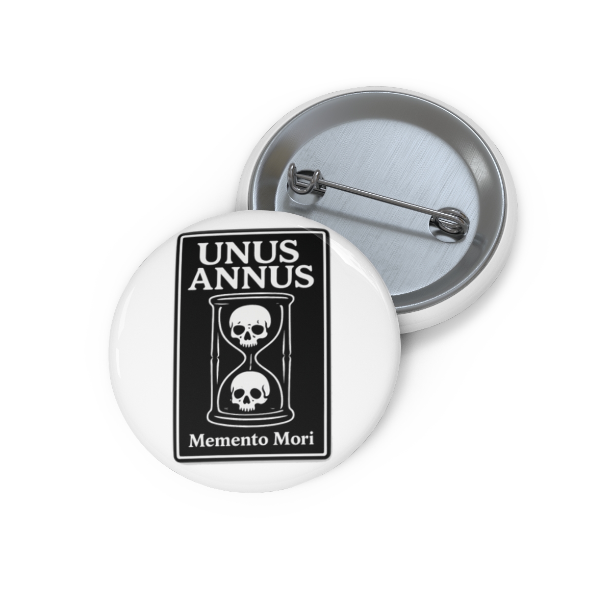 A black and white enamel pin featuring an hourglass with two skulls inside. The pin is on a brown card with the words "Unus Annus" and "Memento Mori" printed on it.